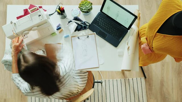 Zoom-in time lapse of clothes designer using sewing machine and measuring handmade garment on dummy working alone at home using laptop