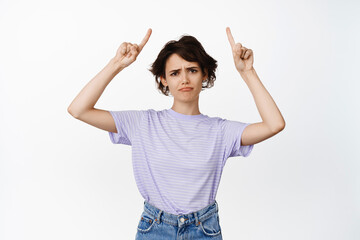 Disappointed brunette girl, woman sad about smth unfair, pointing fingers up, sulking and grimacing...