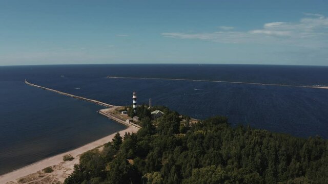 Aerial view of the lighthouse and mole at river Daugava in Latvia. Flying over river that meets the sea.
