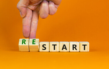 Start or restart symbol. Businessman turns wooden cubes and changes the word 'start' to 'restart'. Beautiful orange table, orange background. Business, start or restart concept. Copy space.