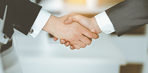 Unknown businessman shaking hands with his colleague or partner while standing straight in sunny office, close-up