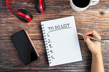 Hand writing To Do List Text on Note pad on top of desk with smartphone and cup of coffee