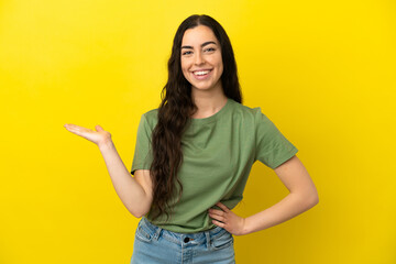 Young caucasian woman isolated on yellow background holding copyspace imaginary on the palm to insert an ad