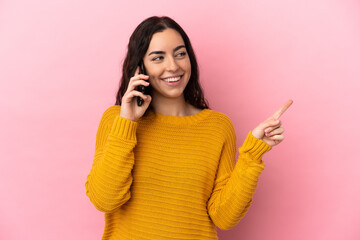 Young caucasian woman using mobile phone isolated on pink background pointing up a great idea