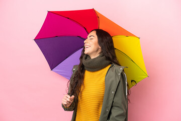 Young woman holding an umbrella isolated on pink background laughing in lateral position