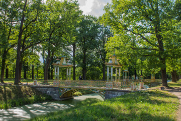 an elegant bridge over the canal in the Tsarskoye Selo Park and bright green trees and grass on a sunny summer day. Concept-walking and tourism in Leningrad region Russia