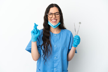 Young woman dentist holding tools isolated on white background with fingers crossing and wishing the best