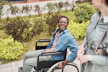 Happy disabled young African-American man in glasses using manual wheelchair and talking to woman during date