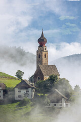 Fototapeta na wymiar Small photogenic stone catholic church in Italian village with dramatic fog