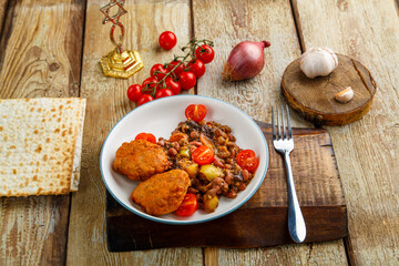 Cod cutlets with stewed potatoes and vegetables on a plate next to matzo and ingredients.