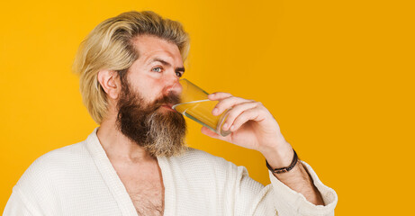 Bearded man with glass of water. Male in bathrobe drinking mineral water In Morning. Healthy...
