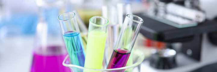 Multi-colored test tubes with liquids stand next to microscope
