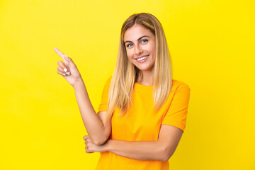Blonde Uruguayan girl isolated on yellow background happy and pointing up