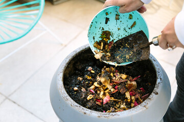 Woman doing compost in the backyard of his house. She is throwing waste of vegetables in the...