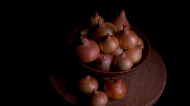 Pile of whole bulbs of raw onion in ceramic bowl on table. Harvest of unpeeled vegetables on black background