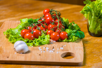 Fresh cherry tomatoes with green salad and garlic on a cutting board.