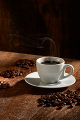 Tasse de café isolée sur fond de bois rustique, verticalement avec des groupes de grains de café sélectionnés autour.