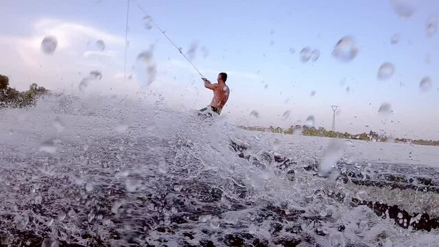 SLOW MOTION CLOSE UP Man is riding a wakeboard on the water. Splashes fly in different directions.