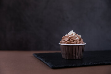 Delicious chocolate cupcake with cream and white chocolate sprinkling on a dark background. Sweets for a party.