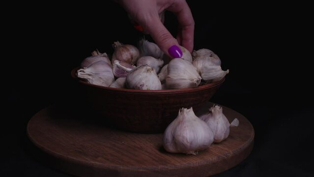Pile of whole bulbs of garlic in ceramic bowl on table. Woman's hand takes garlic from bowl