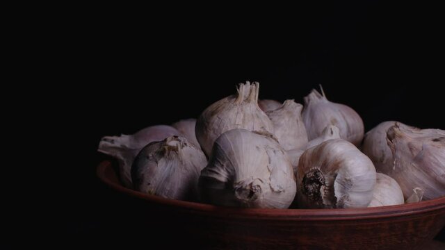 Pile of whole bulbs of garlic in ceramic bowl on table. Harvest of unpeeled vegetables on black background.