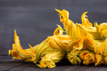 Raw zucchini flower concept: Fine dining cuisine of edible fresh and organic flowers. Healthy lifestyle ingredients. Close-up on yellow vegetables on black background with large copy space.