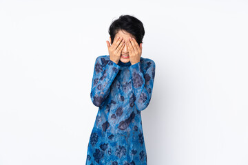 Young Vietnamese woman with short hair wearing a traditional dress over isolated white background covering eyes by hands