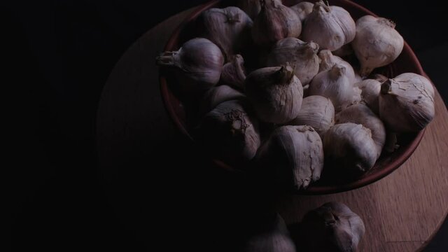 Pile of whole bulbs of garlic in ceramic bowl on table. Harvest of unpeeled vegetables on black background