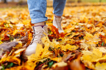 Legs of unrecognosable woman wearing brown boots and jeans in autumn yellow foliage walking in park or forest - Powered by Adobe