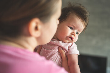 Over the shoulder view on young caucasian mother holding her four months old caucasian baby girl daughter in room at home in summer day real people motherhood and parenting concept copy space