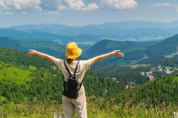 Traveler with a backpack stands with her arms outstretched in the mountains in summer. The top of the mountain evokes good or uplifting mood