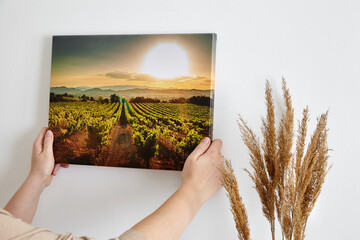 Canvas print with gallery wrap and dry grass interior decor. Woman hangs landscape photography on...