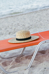 Straw hat and orange sunbed on sand beach, no people. Idyllic and tranquil summer vacation concept.