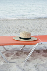 Straw hat and orange sunbed on sand beach, no people. Idyllic and tranquil summer vacation concept.