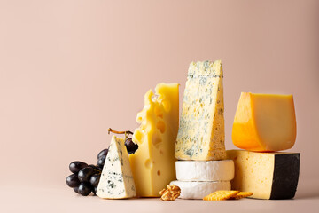 Different types of cheese on pastel pink light background. Cheeses mix maasdam, cheddar, dor blue, gorgonzola, camembert, brie and grapes, walnuts, galeta.