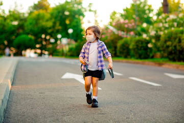 Fototapeta premium a beautiful little girl, a schoolgirl, is standing on the road, with a backpack, holding a diary in her hands