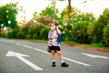 a beautiful little girl, a schoolgirl, is standing on the road, with a backpack, holding a diary in her hands