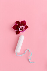 Orhid and tampon on pink background. Female health, menstruation concept. Flower as symbol of vagina.