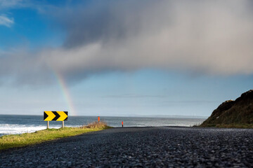 Arrow direction sign pointing to colorful rainbow over Atlantic ocean, Mullaghmore, county Sligo, Ireland. Blue cloudy sky. Nobody