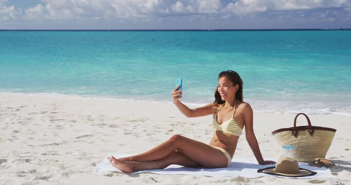 Summer beach vacation girl taking mobile phone selfie photo with. Cute Asian woman wearing posing for phone self-portrait photo enjoying suntan on tropical travel holidays