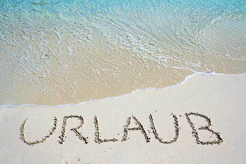 Urlaub am Strand. Im Sand vor dem Meer steht das Wort Urlaub