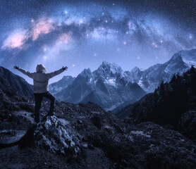 Naklejka na ściany i meble Arched Milky Way, sporty man on the stone and mountains in snow at starry night. Happy young man, sky with bright stars, snowy rocks in Nepal. Space. Landscape with milky way arch. Travel and hiking