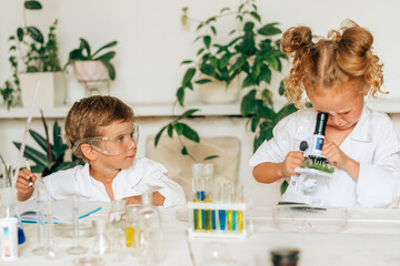 Boy and girl in white uniforms and protective glasses do chemical experiments in a home...