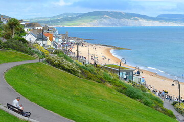 Man waiting on a bench overlooking the ammonite fossil shaped lamp posts along the promenade Lyme's sheltered south-facing beach is ideal for kids to play and adults to relax in the classic deckchairs © Rusana