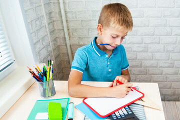 The boy writes on the blackboard with a marker. Office supplies are laid out on the table. Back to school.