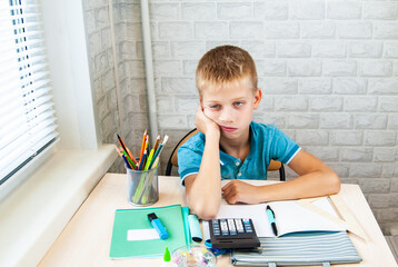 Boy, tired of lessons, is sitting at school desk with his head down. Office supplies are laid out on the table. Back to school.