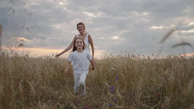 Daughter and mother dream together run in the wheat field at sunset. happy family people in the wheat field concept. Mom and girl playing catch-up run. baby child fun running in green meadow. 