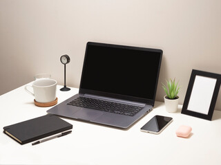 Fototapeta premium Picture of laptop on a white table with a mug a clock a small bush a notebook a phone a picture frame and a headphone case