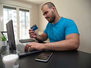 Young man working from his living room on a laptop on a black table with a white candle his phone and a credit card with a black notebook