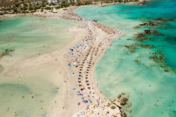 Aerial view of sunshades and umbrellas on a narrow sandy beach surrounded by shallow lagoons (Elafonisso Beach, Crete, Greece)